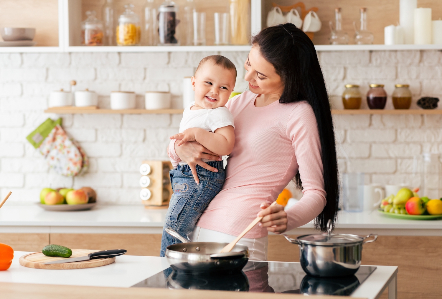 A,Woman,Is,Standing,In,A,Kitchen,,Holding,A,Baby.